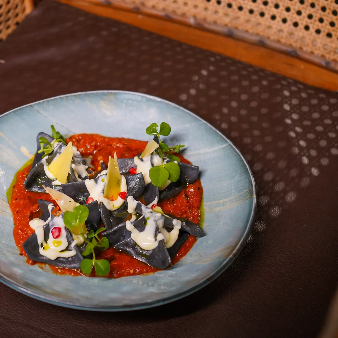 Black ravioli served on a rich red sauce, topped with cream, microgreens, and garnishes at a Bangalore brewhouse.