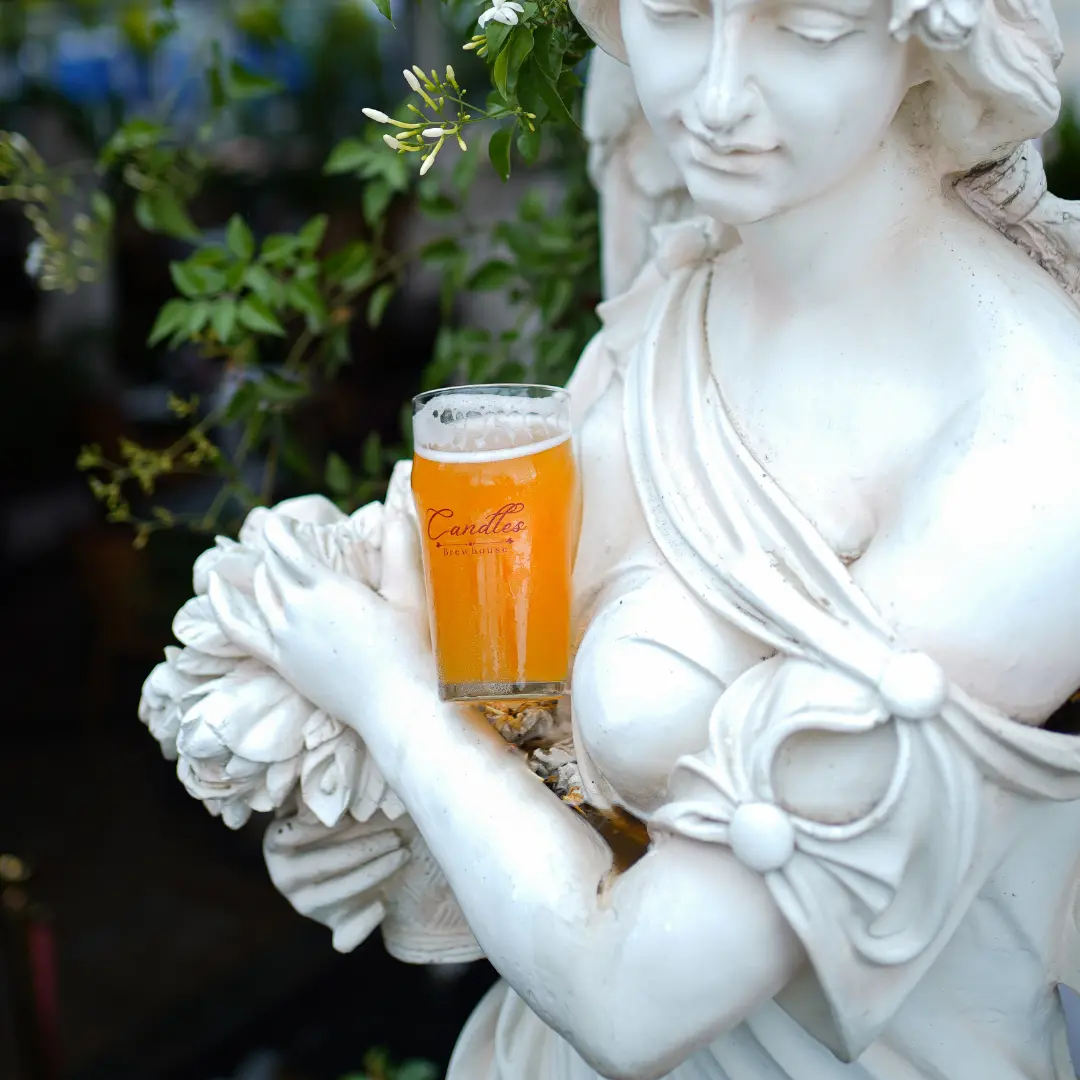 A pint of craft beer placed in the arms of a white marble statue at a Bangalore brewhouse.