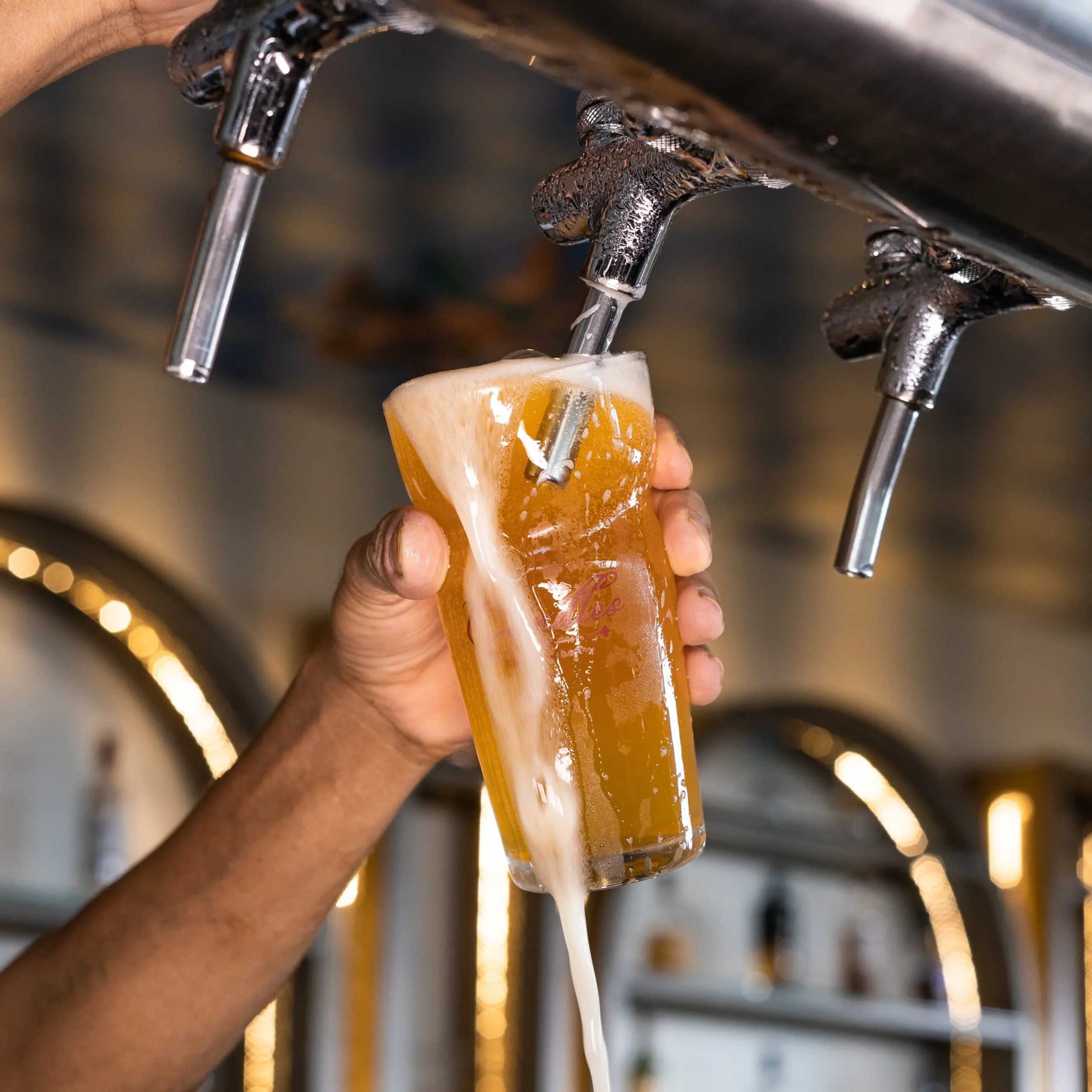 Hand pouring a freshly tapped draft beer into a glass with foam overflowing from the tap.