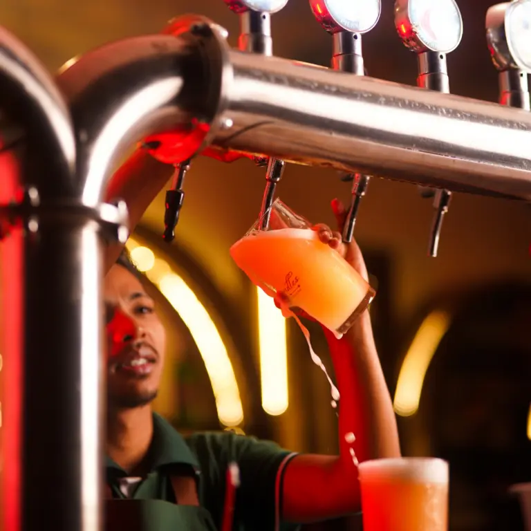 Bartender pouring a fresh craft beer from the tap into a glass with foam overflowing at a Bangalore brewhouse.