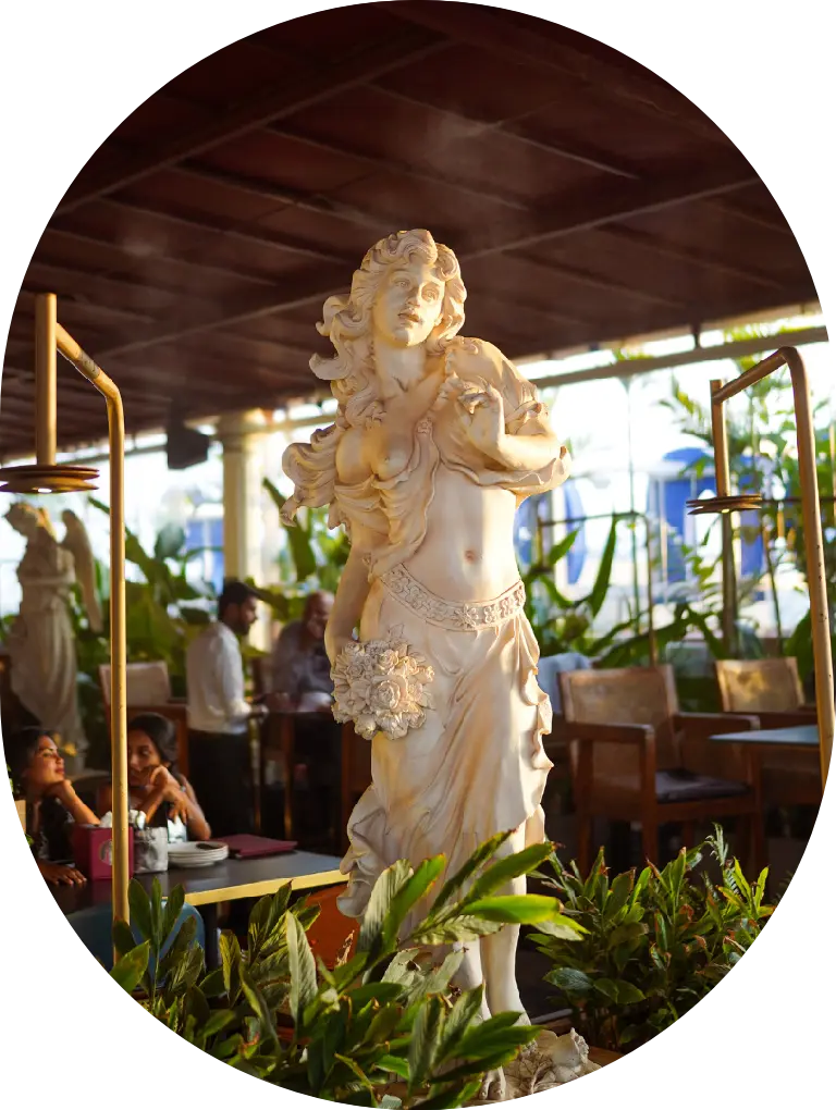 Elegant marble statue surrounded by greenery inside a beautifully lit brewhouse in Bangalore.
