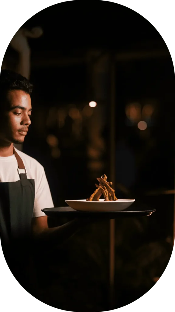 Server presenting a gourmet dish on a tray at Candles Brewhouse during nighttime service.